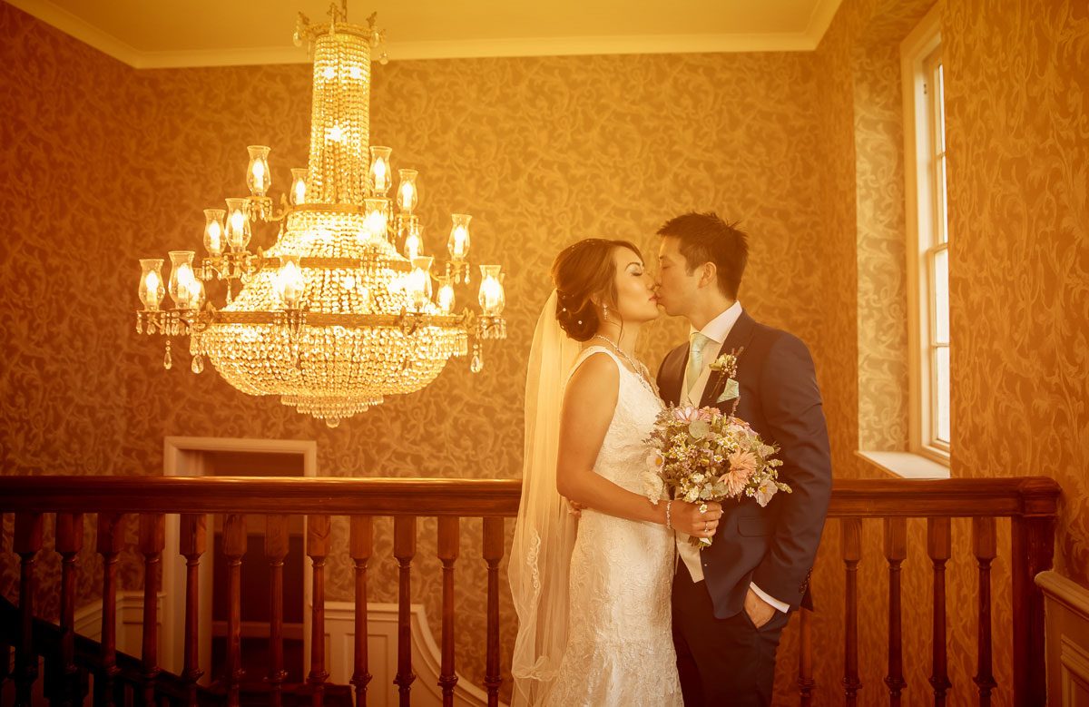 Wedding couple kiss by chandelier at Stoke Place Hotel