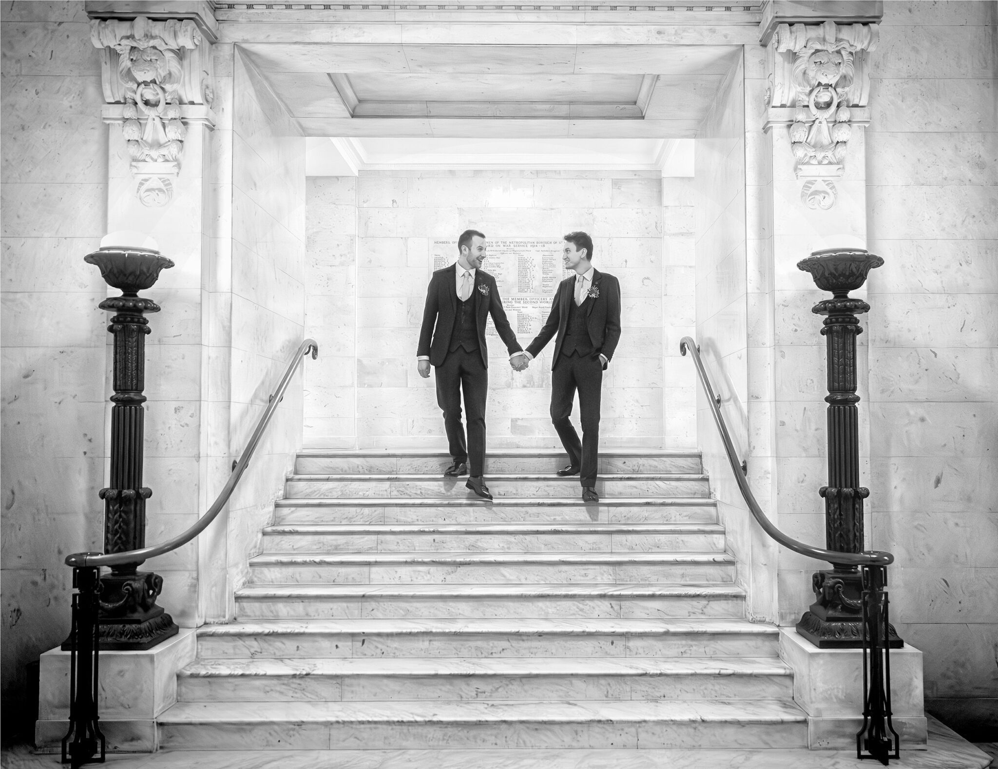 Two grooms hand in hand down stairs Old Marylebone Town Hall