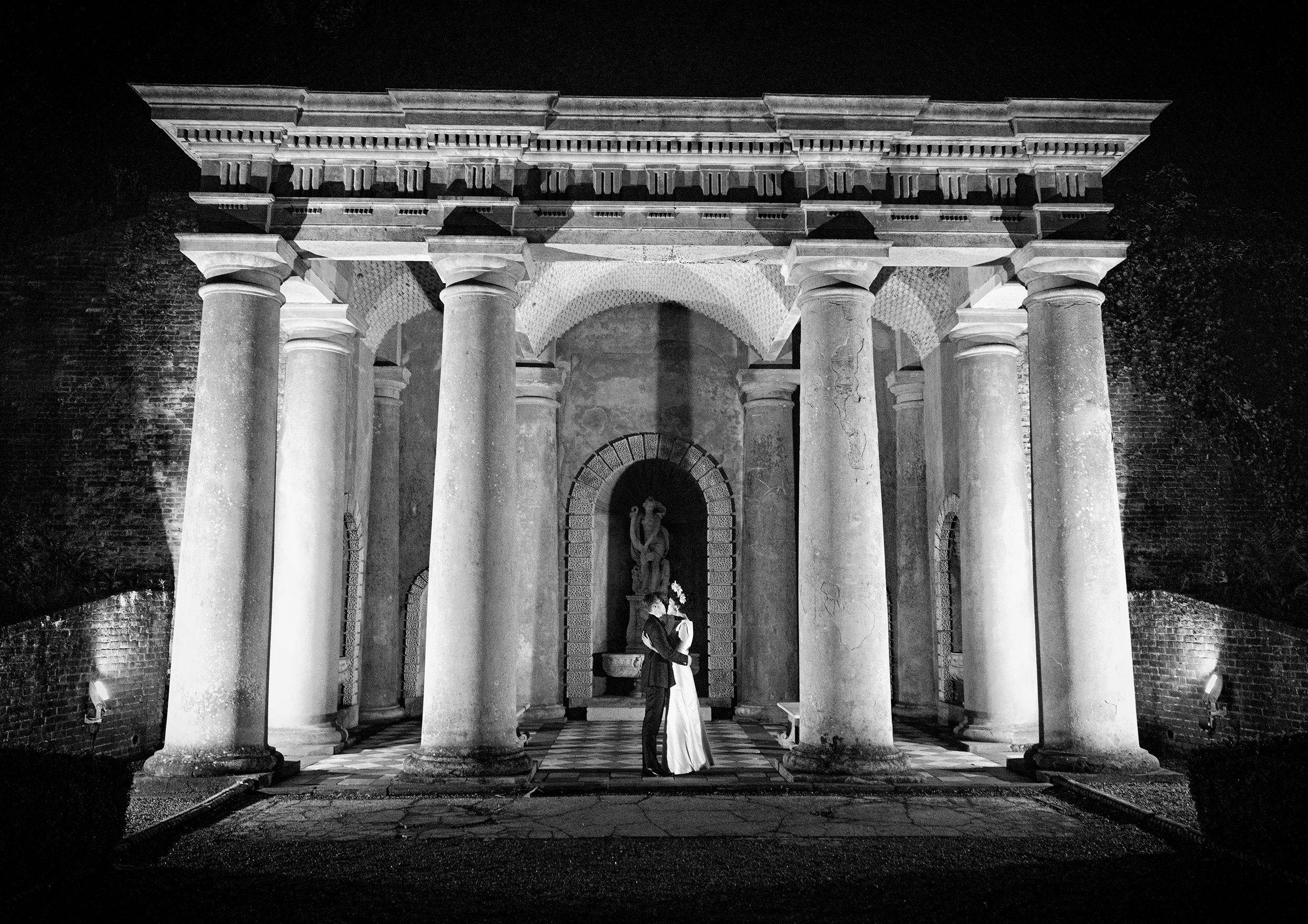 Bride and groom kiss at night after wedding between pillars Wotton House