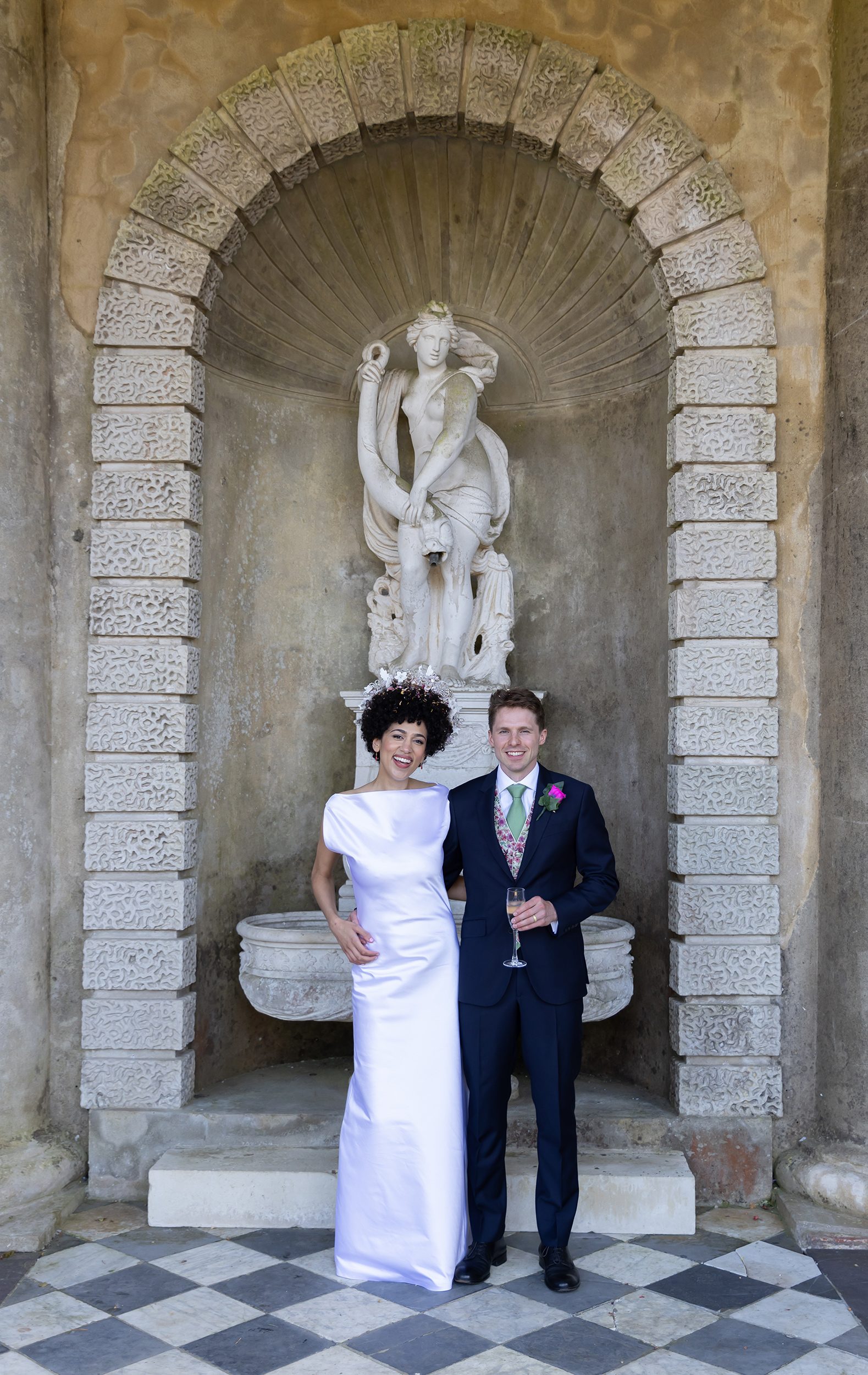 Bride and groom smile by statue Wotton House