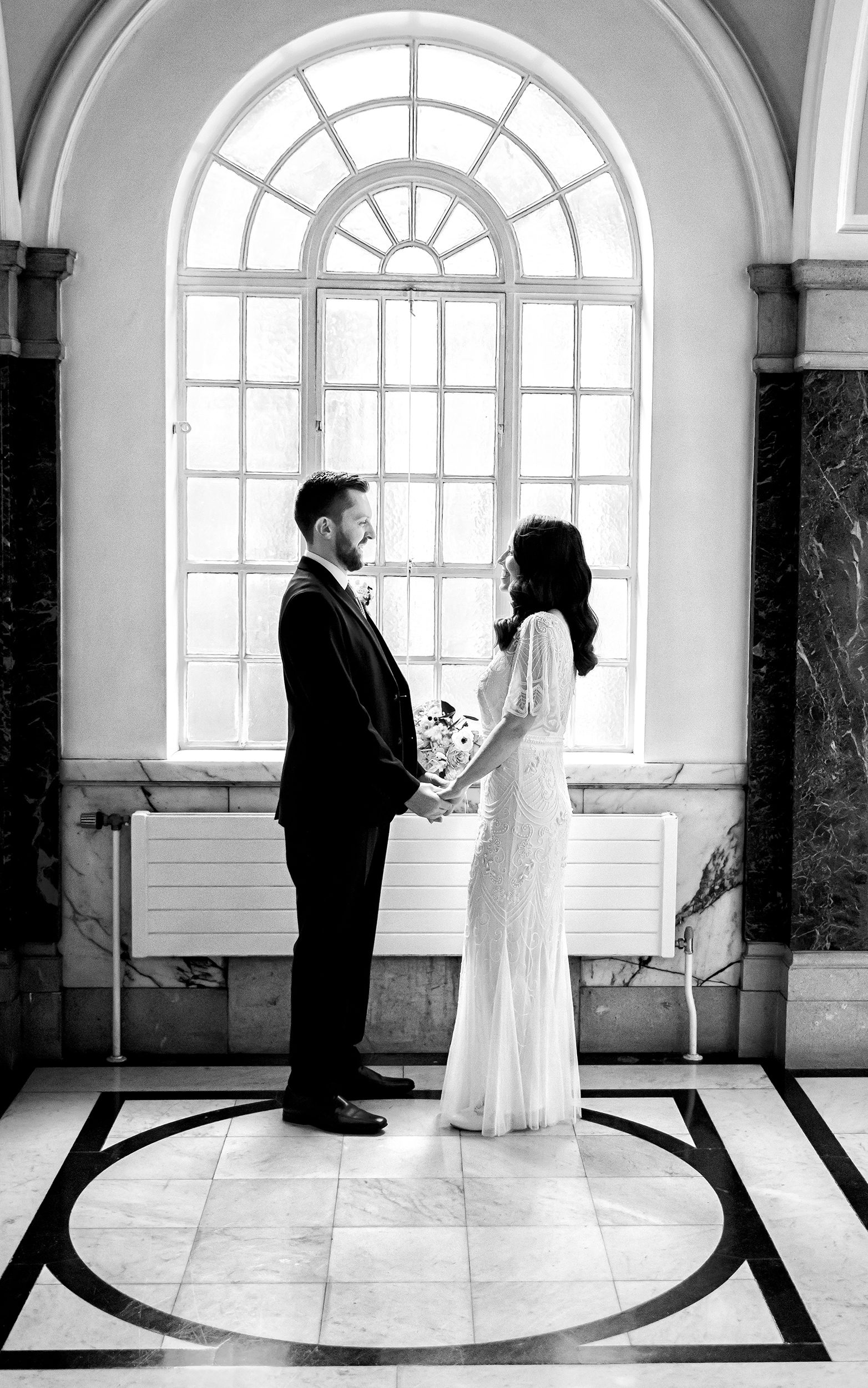 Bride and groom hold hands by Islington Town Hall window